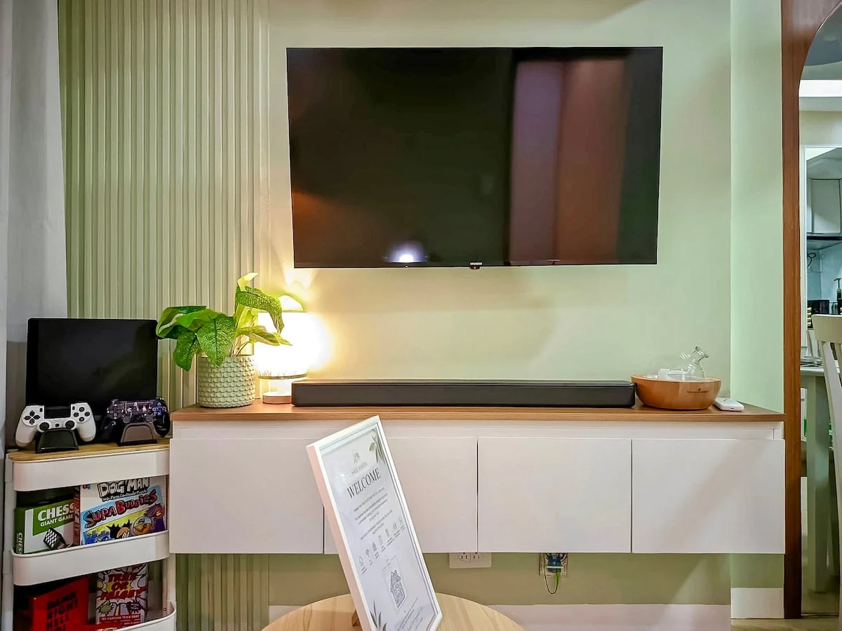 Wall-mounted TV above a white console, with a PS4 and board games beside it