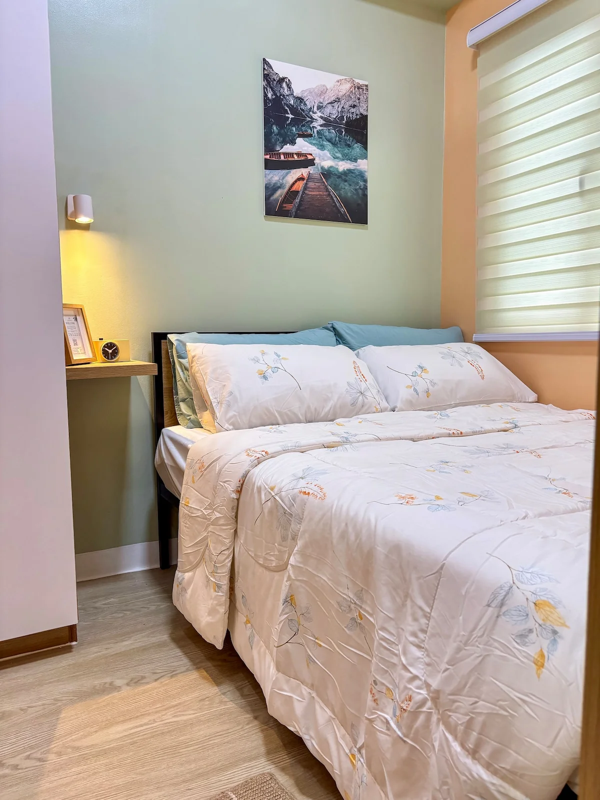 Queen bed beside a wood bedside table, with wall art and a window