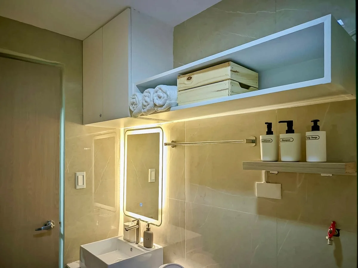 Bathroom sink, illuminated mirror, rolled towels and toiletries